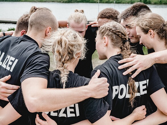 Auf dem Foto ist eine Gruppe von Studierenden zu sehen, die im Kreis stehen, sich umarmen und sich anfeuern.