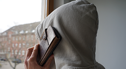 Rückansicht einer Person mit Kapuzenpullover und Mobiltelefon in der Hand