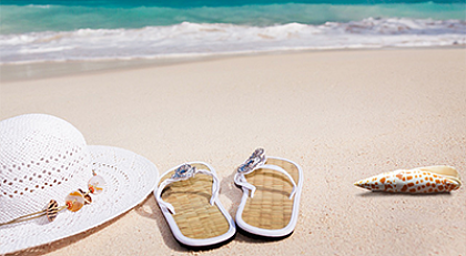 Badelatschen, Sonnenhut und Muschel am Strand 