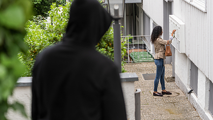 Männliche Person beobachtet aus der Ferne eine Frau am Briefkasten eines Wohnhauses