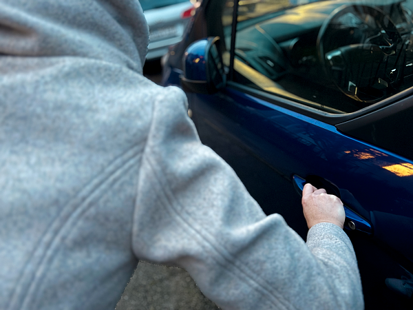 Person, die gebeugt vor der Fahrertür eines Autos steht und die Fahrertür mit der Hand ergreift