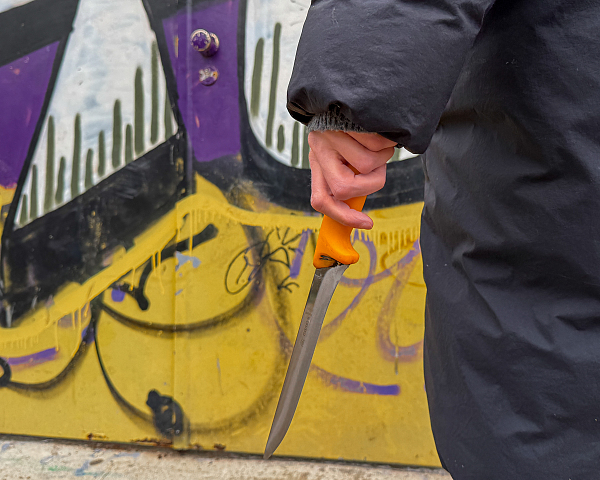 Person steht vor Graffiti Wand und hält ein Messer in der Hand